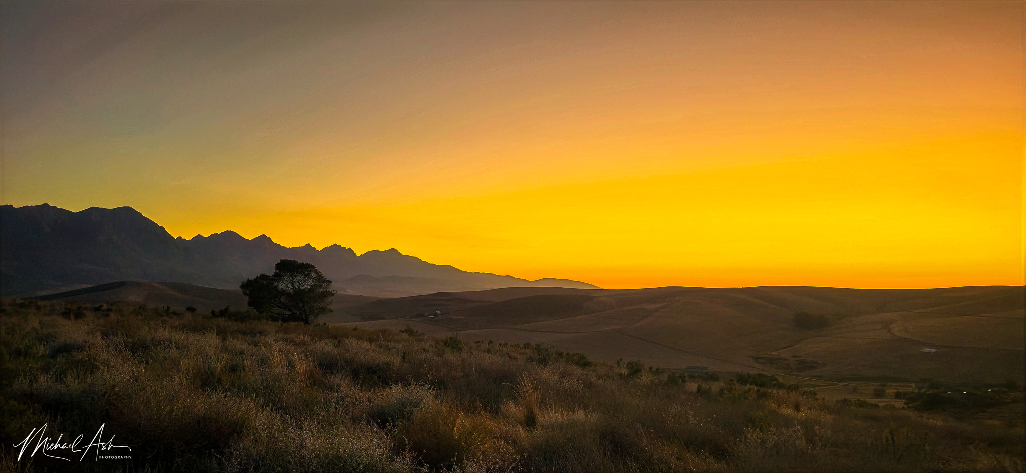 Landscape & Views Golden sunset over Riviersonderend Mountain Range with indigenous fynbos vegetation in foreground, showing dramatic orange and pink sky with layered mountain silhouettes