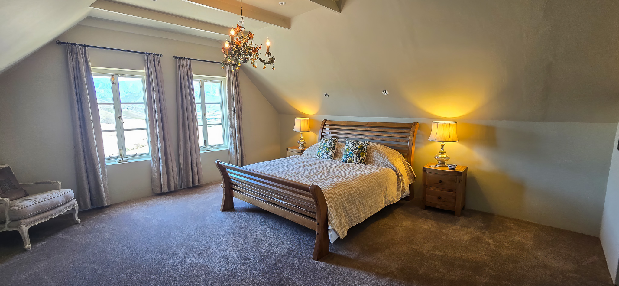 Interior Spaces Second bedroom interior showing vaulted ceiling with exposed beams, crystal chandelier, wood sleigh bed, warm lighting, and mountain views