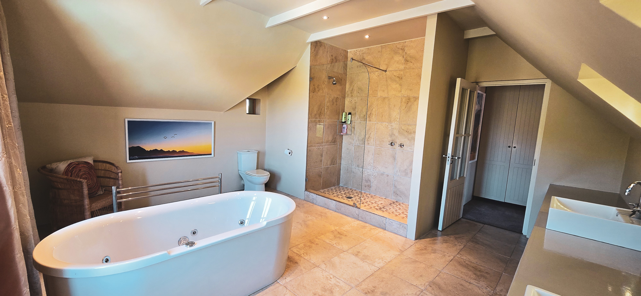Interior Spaces Second bedroom en-suite bathroom featuring freestanding bathtub, walk-in shower, stone tiles, exposed beams, and mountain artwork