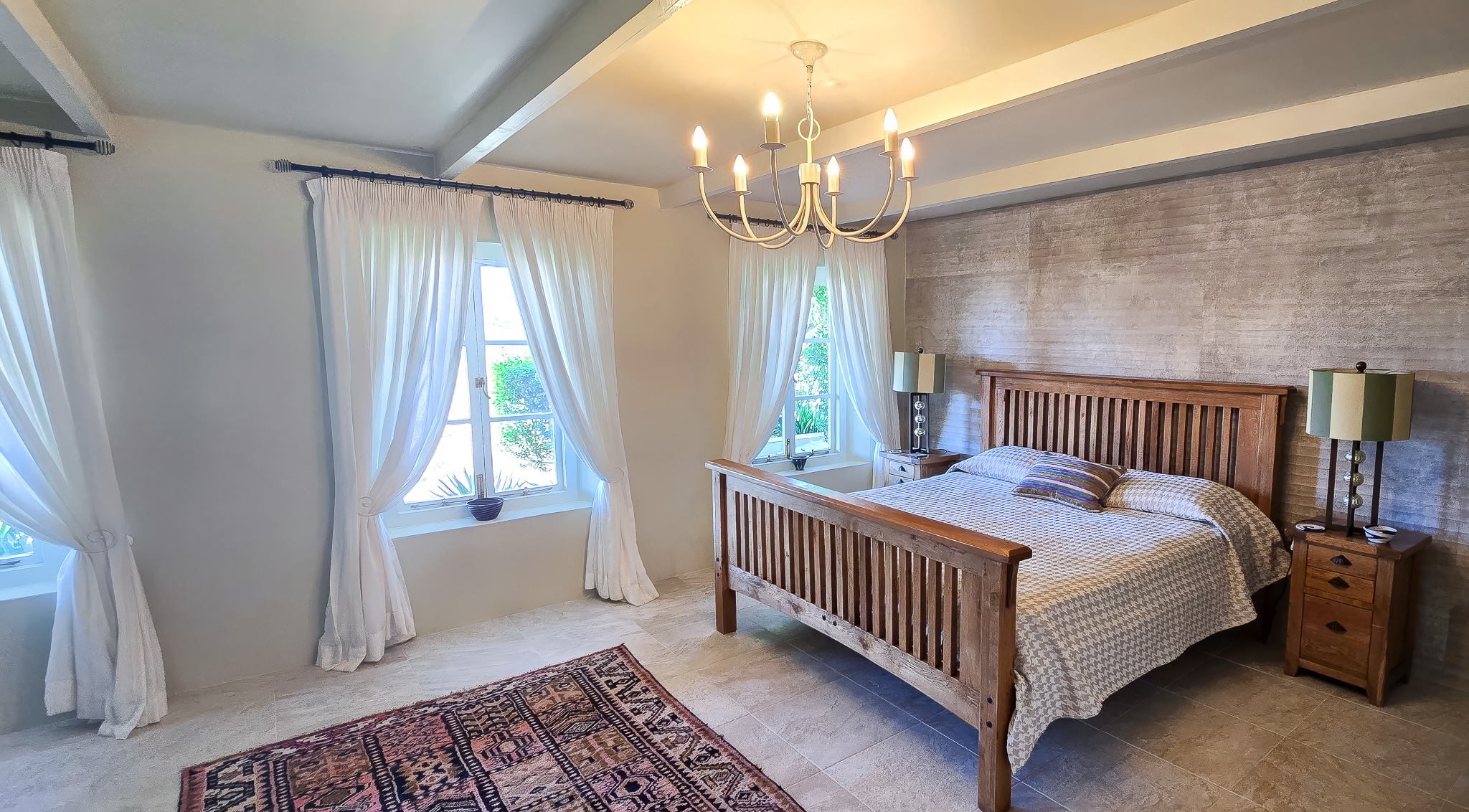 Interior Spaces Third bedroom interior showing exposed beam ceiling, chandelier, wood furniture, brick accent wall, and elegant decor