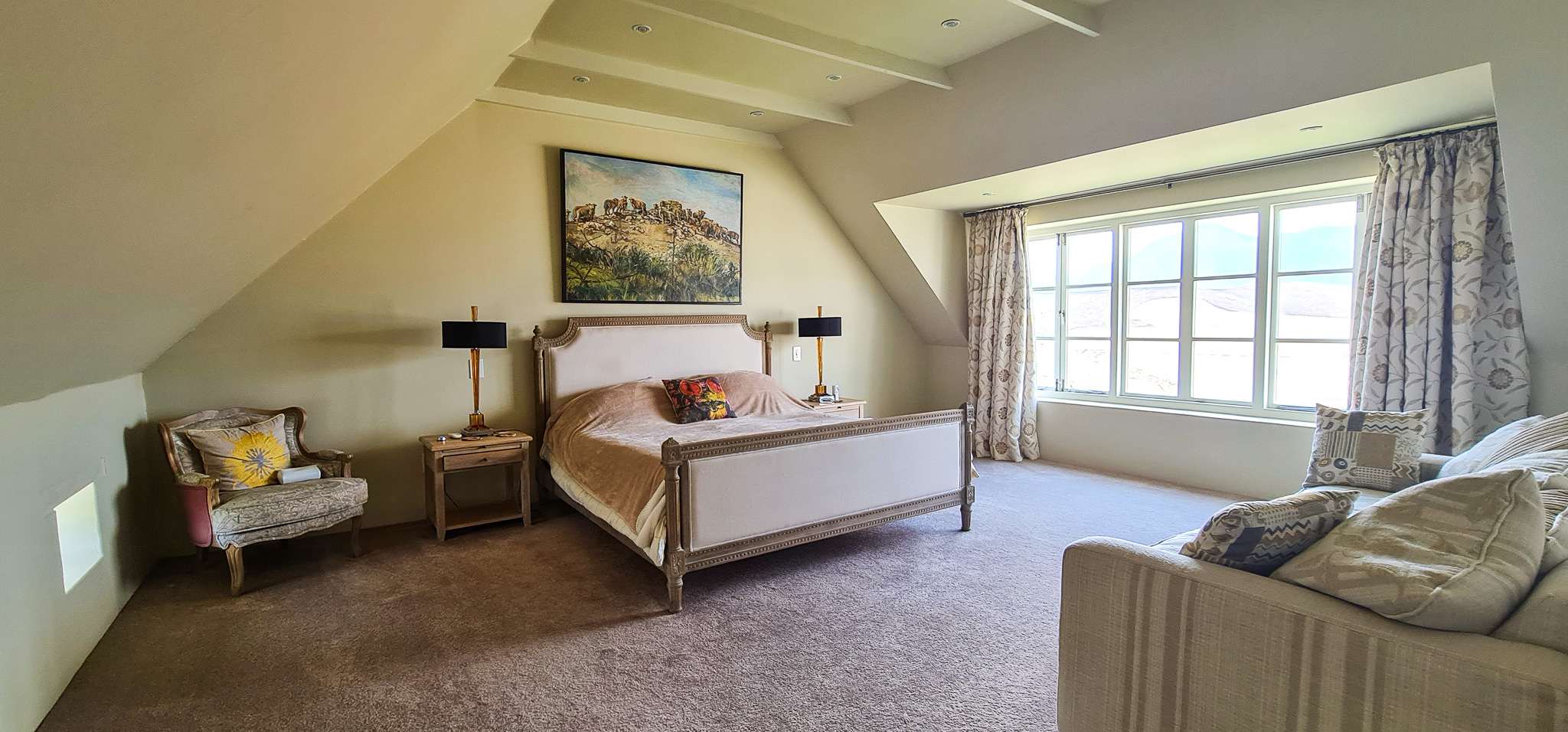Interior Spaces Spacious master bedroom featuring vaulted ceiling with exposed beams, wood furniture, comfortable seating area, large windows with natural light, and mountain landscape artwork