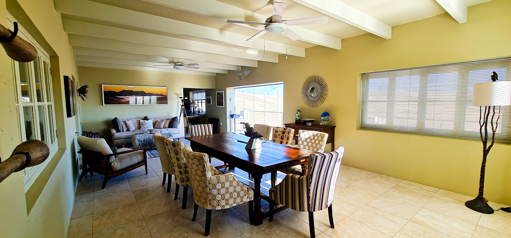 Interior Spaces Spacious dining room featuring exposed beam ceilings with ceiling fans, yellow accent walls, large dining table with patterned chairs, and open floor plan connection to living areas