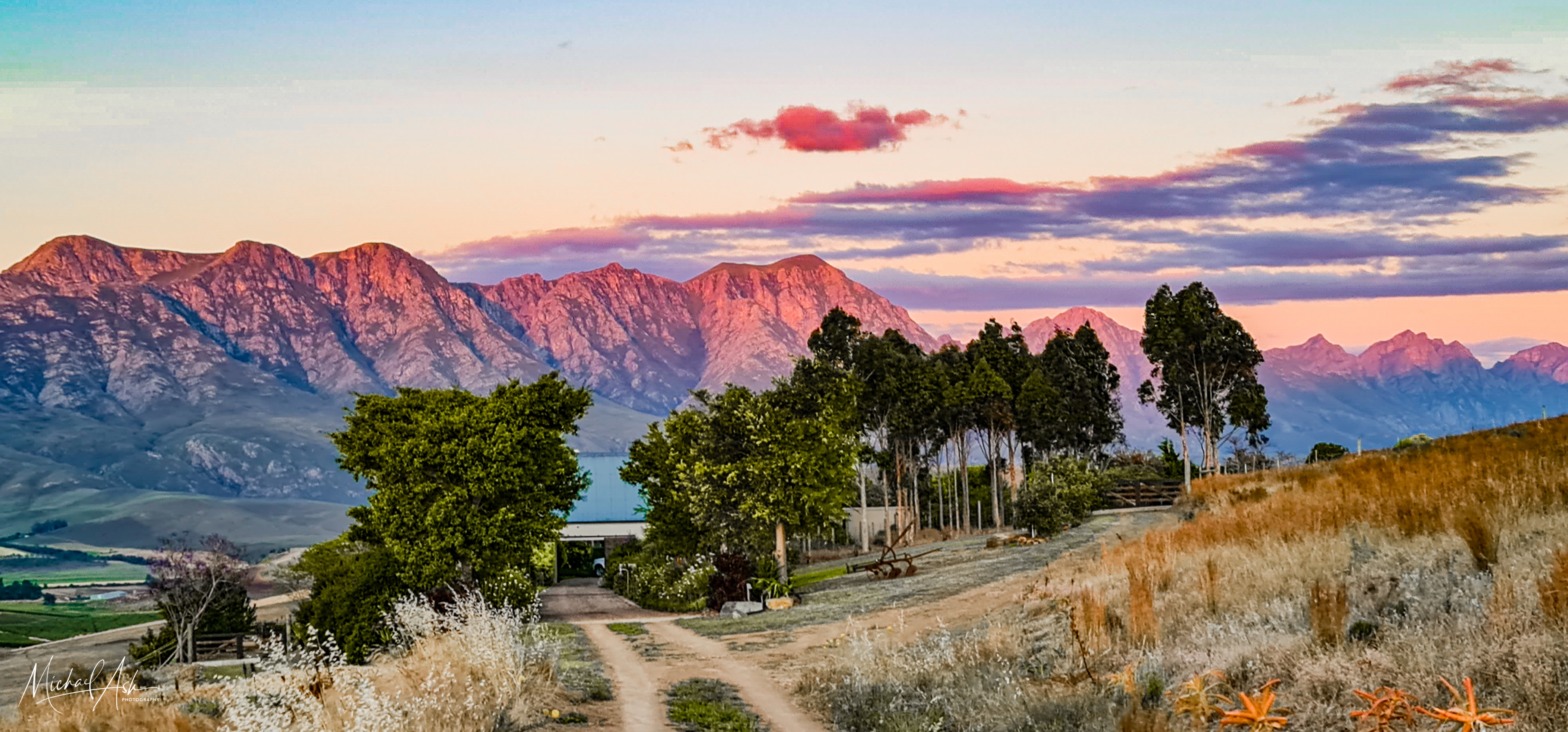 Landscape & Views Dramatic sunset landscape showing mountain ranges, golden grasslands, and spectacular sky at farm entrance