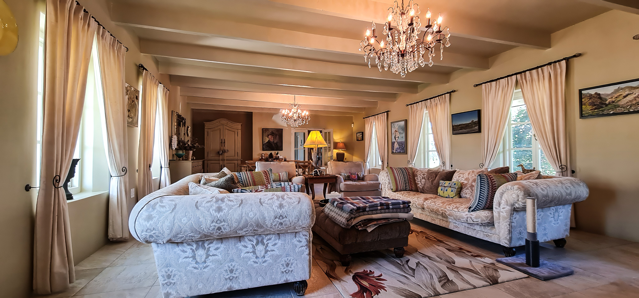 Interior Spaces Elegant main lounge showing exposed beam ceilings, crystal chandeliers, comfortable seating with patterned fabrics, large windows with curtains, and warm lighting