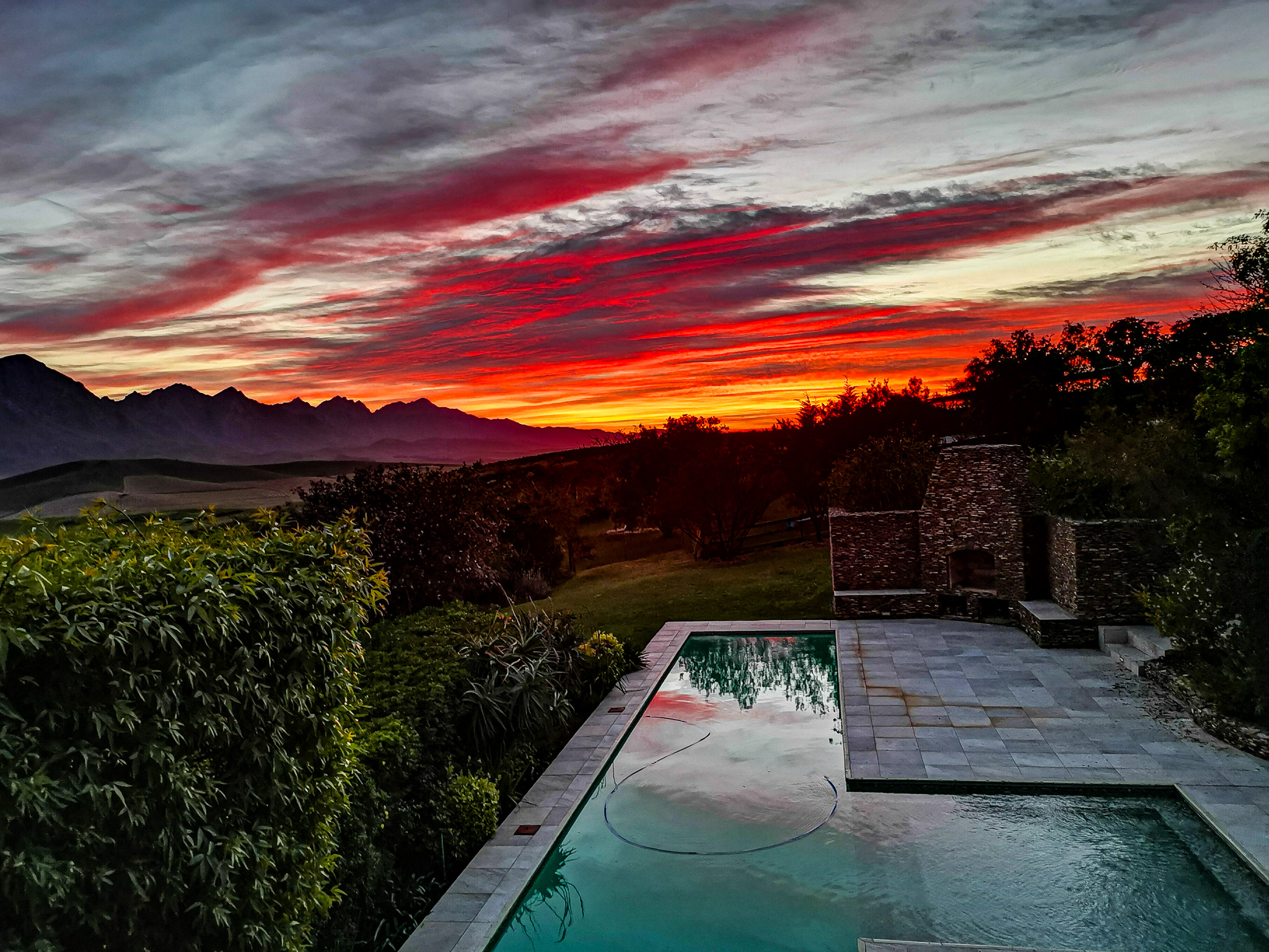 Exterior & Architecture Stunning sunset pool view showing the swimming pool with dramatic red, orange and pink sunset clouds over the Riviersonderend Mountain Range reflected in the water