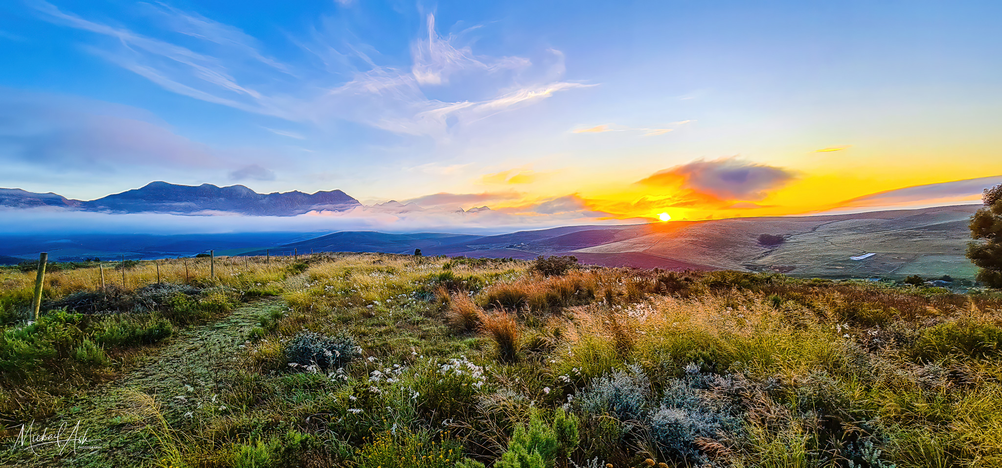 Landscape & Views Spectacular spring landscape showing dramatic sunset with vibrant orange sky, layered mountain ranges with mist, and native Renosterveld vegetation