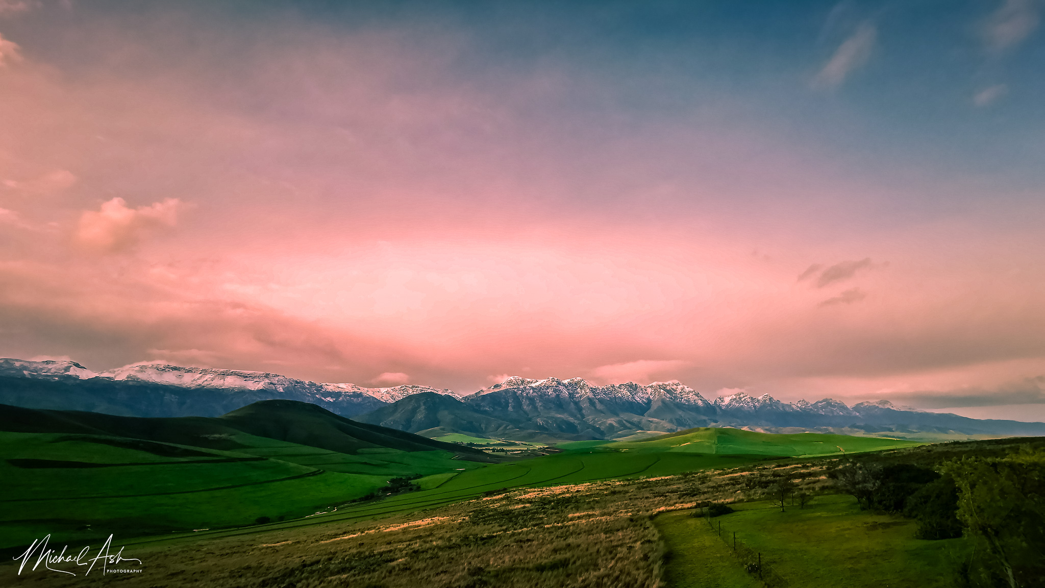 Landscape & Views Winter landscape showing snow-capped mountain ranges under dramatic pink and purple sunset sky with green Overberg countryside